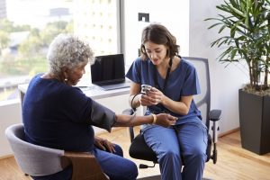 Nurse Wearing Scrubs In Office Checking Senior Female Patients Blood Pressure