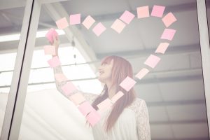 Smiling hipster woman doing a heart in post-it in office