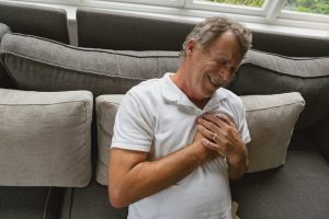 Active senior Caucasian man suffering from chest pain on sofa in a comfortable home