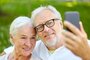 senior couple with smartphone taking selfie in summer